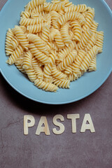 White fusilli pasta cooked and served on a blue plate on a grey background