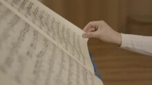 Female Hand Flip Through Notes On Music Stand, Background Of Room Interior. Gimbal Closeup Shot Of Classical Music Notes In Paper Leaf Through On A Stand