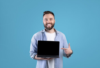 Poster - Portrait of happy bearded man holding laptop computer with empty screen over blue studio background, mockup for design