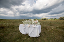 Table With White Tablecloth, Candlestick And Wildflowers In The Field
