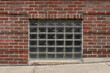 Straight on view of a basement window with glass brick blocks inset, concrete sidewalk on an incline, horizontal aspect