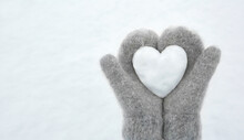 Women's Hands In Light Gray Knitted Mittens Hold A Beautiful White Heart Made Of Snow