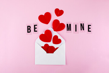 White envelope, red paper hearts and text Be Mine on pink background. Valentine's day, love concept