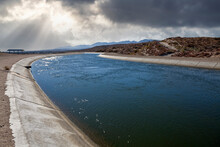 View Of The California Aqueduct Water Canal With Storm Sky In The Mojave Desert.  