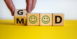 Good mood symbol. Male hand flips a wooden cube and changes the word 'good' to 'mood'. Positive smiles. Beautiful yellow table, white background, copy space. Business and good mood concept.