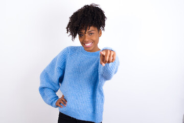 Wall Mural - Young beautiful African American woman wearing blue knitted sweater against white wall pointing at camera with a satisfied, confident, friendly smile, choosing you