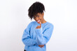 © Roquillo - Young beautiful African American woman wearing blue knitted sweater against white wall Beckoning come here gesture with hand inviting welcoming happy and smiling