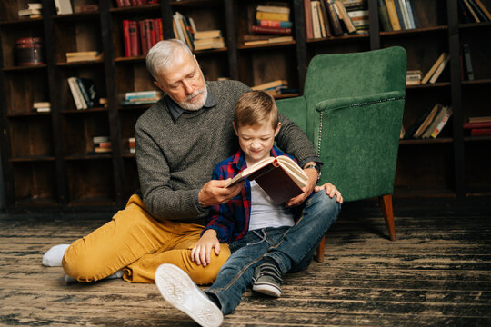 senior grandfather and little grandson reading interesting book together sitting on floor on home li