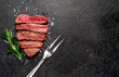 Different degrees of roasting beef steak in the shape of a heart with spices and a meat fork on a stone background with copy space for your text.