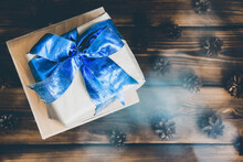 Beautiful Gift In Craft Paper With A Blue Bow On A Wooden Background. Christmas Mood