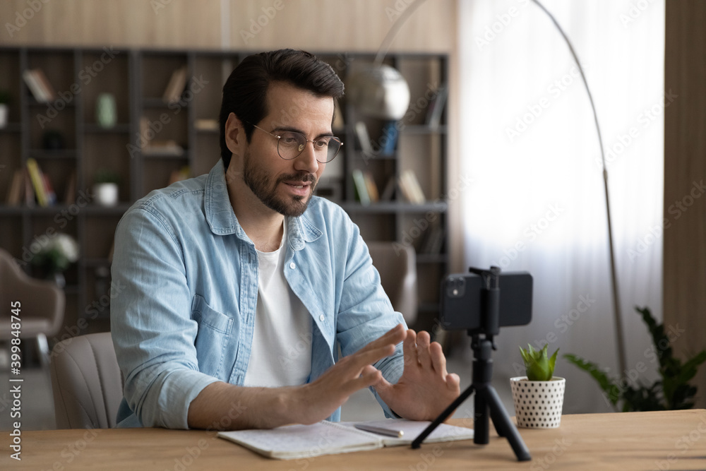 Millennial Caucasian male coach or speaker record live broadcast on smartphone camera at home. Young man tutor talk speak on video call or webcam digital conference on cellphone. Training concept. - obrazy, fototapety, plakaty 