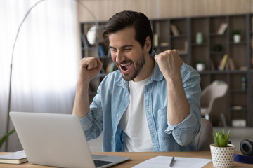 Wall Mural - Excited young Caucasian man look at laptop screen feel euphoric celebrate online lottery win. Overjoyed millennial male triumph reading good news on computer, get promotion email letter. Luck concept.