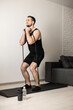 © Ivan - Fit man performs exercises using a resistance band. Hard workout at home. Minimalistic interior on background. Water bottle near yoga mat. A man gets pleasure from doing his favorite exercise.
