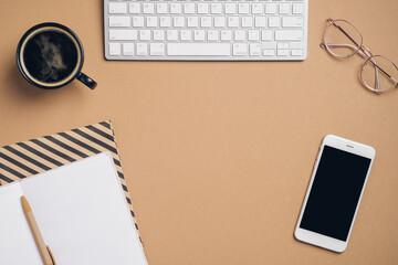 Fototapete - Flatlay computer keyboard, cup of coffee, glasses, phone with blank screen mockup, paper notebooks on pastel beige background. Elegant feminine workspace, home office desk table.