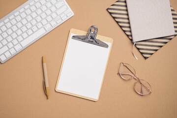 Fototapete - Modern home office desk top view with blank clipboard, computer keyboard, glasses, pen, paper notebook on pastel brown background. Elegant blogger workspace. Business concept.