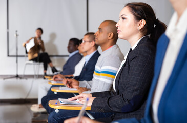 Canvas Print - Confident young woman attentively listening to lecture with colleagues at business conference