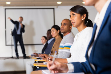 Wall Mural - Portrait of young focused woman sitting and listening to speaker at business conference