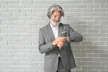 Wall Mural - Mature man in formal suit with wrist watch on brick background