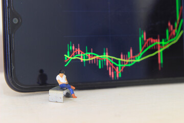 Wall Mural - Simple Conceptual Photo, illustration for Young Man Investor Mini Figure Toy businessman Seriously watching Running Stock Exchange Sitting at stappler