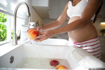 Canvas Print - Young pregnant woman washing fresh sweet peach in kitchen, closeup. Taking care of baby health