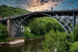 The Iron Bridge is a cast iron arch bridge that crosses the River Severn in Shropshire, England. Opened in 1781, it was the first major bridge in the world to be made of cast iron. Sky added.