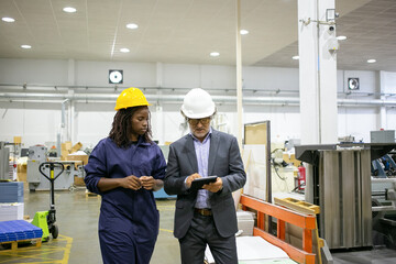 Caucasian manager discussing factory work with African worker. Beautiful pensive young woman working on plant and looking on tablet in supervisor hands. Manufacture and digital technology concept