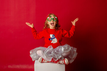 little girl in carnival glasses holds a gift on a red background, christmas