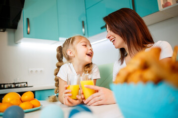 Mother with little girl drinking orange juice while they have breakfast together