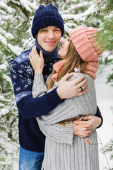 happy woman looking at man in winter forest among fir trees