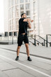 © Ivan - Sporty man stretching arms before jogging. Runner in black sportswear excercising at morning. Healthy lifestyle concept. Morning city on background. Active living. Outdoor fitness.