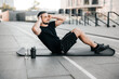 © Ivan - Fit man pumping press lying on black yoga mat. Muscular man doing his favorite morning exercise. Black sport clothes. Fit happy man doing fitness exercises outdoors. Street on background.