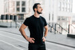 © Ivan - Male runner paused jogging to admire the beautiful morning view of the city. Man in black sportswear holding his hands at waist and looking away. Urban sport concept. Morning workout.
