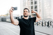 © Ivan - Attractive man shows biceps and takes a selfie. Social media concept. Male athlete in black t-shirt shows to friends on a videocall his fit body. Morning workout. Urban sport concept.