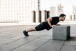 © Ivan - Sporty man pushing from stone cube with legs on asphalt. Workout outdoors. Man in black sportswear exercising at morning. Strong man excercising to have a fit body. Fitness. City on background.
