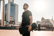 © Ivan - Confident young man holding rolled yoga mat and looking at beautiful morning view of big city. Morning activities concept. Bright sunshine on background. Black sporswear.