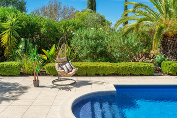 Luxurious pool in the garden of a private villa, hanging chair with pillows for leisure tourists, in summer. Portugal, Algarve.