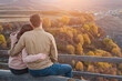 © lenblr - Young couple hugs sitting on bench on viewing point against picturesque ancient mountains at sunset backside view