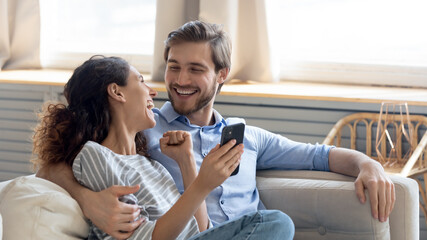 Wide banner panoramic view of overjoyed millennial couple celebrate online win on cellphone together. Happy young Caucasian man and woman triumph with good sale deal or promotion discount on cell.