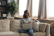 © fizkes - Happy dreamy young Caucasian woman sit rest on couch at home work on laptop look in distance thinking dreaming. Thoughtful millennial female use computer visualize or imagine future success.