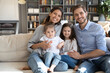 © fizkes - Portrait of happy young Caucasian family with two daughters sit relax on couch at home hugging together. Smiling mom and dad rest on sofa with little girls children, enjoy weekend in own house.