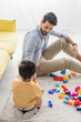 © LIGHTFIELD STUDIOS - Hispanic father playing building blocks near son on blurred foreground, two generations of men