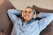 © Ivan - Middle aged man listening to music, lying on sofa with closed eyes and smiling with teeth. Casual style. Man enjoying his favorite music and relaxing at home. Spending time during quarantine.
