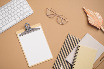 Fototapete - Flat lay home office desk. Feminine workspace with computer keyboard, clipboard, glasses, paper notebooks on pastel brown background. Top view blogger workspace. Business concept.