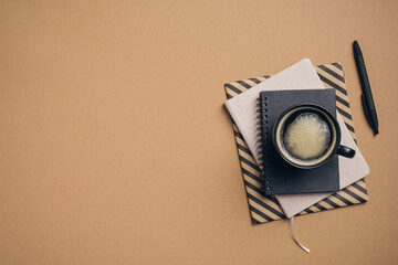Poster - Office table with cup of coffee, paper notebook, notepad, pen on brown background. Top view with copy space, flat lay. Business, coffee break concept.