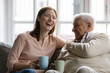 © fizkes - Family members of two generations grown daughter and mature father having fun enjoy tea talk on cozy couch. Attentive young lady caregiver social worker visit support care for glad elderly man patient