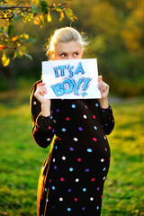 Pregnant woman on second trimester posing in sunny garden, shows a slogan its a boy