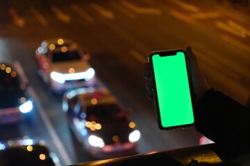 Wall Mural - close up hand holding green screen smart phone with blurred traffic at night