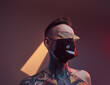 © Fxquadro - Tattooed hipster person weared with black stylish mask and sunglasses poses in dark and colourful room with spotlights with naked torso.