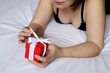 Gift box in female hands, woman opens red packaging with present lying on a bed. Concept of birthday, Christmas celebration, Valentine's day