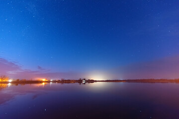 A magical starry night on the river bank with a large tree and a milky way in the sky and falling stars in the summer.	